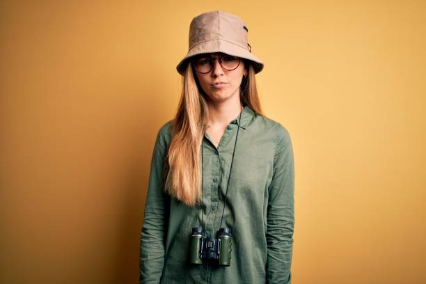 istock Beautiful blonde explorer woman with blue eyes wearing hat and glasses using binoculars depressed and worry for distress, crying angry and afraid. Sad expression. 1212512822