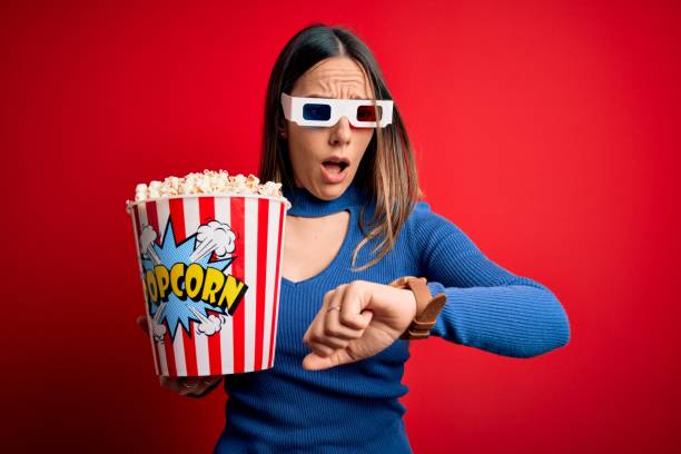 giovane donna bionda che indossa occhiali 3d e mangia confezione di popcorn guardando un film al cinema guardando il tempo dell'orologio preoccupato, paura di arrivare in ritardo - checking the time women impatient wristwatch foto e immagini stock