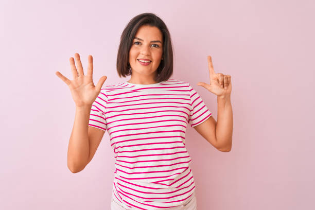 junge schöne frau trägt gestreifte t-shirt steht über isolierten rosa hintergrund zeigt und zeigt mit den fingern nummer sieben, während lächelnd zuversichtlich und glücklich. - hispanic male stock-fotos und bilder