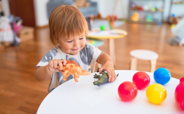 Adorable toddler playing with dinosaurs around lots of toys at kindergarten Adorable toddler playing with dinosaurs around lots of toys at kindergarten jurassic photos stock pictures, royalty-free photos & images