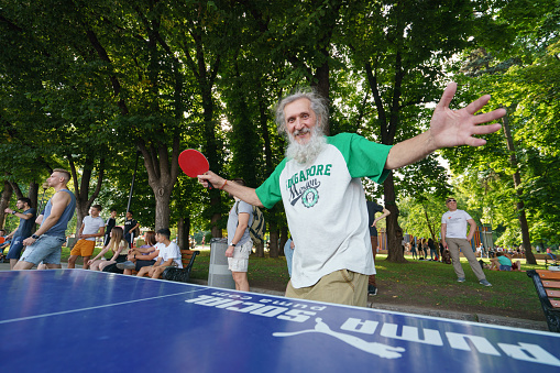 Moscow, Russia - July 27, 2019: Frontal view of bearded old man playing table tennis. Photography of street ping-pong sports competitions in the Gorky park in day.