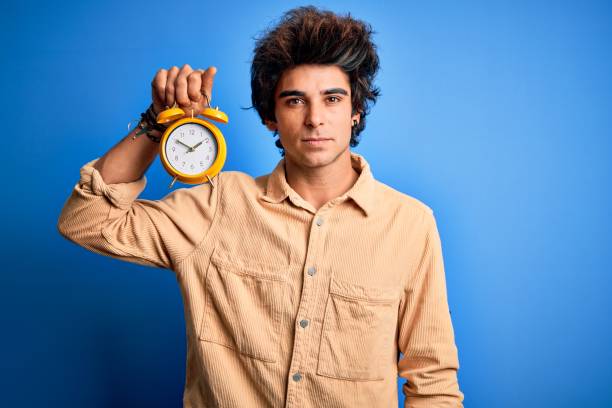 istock Young handsome man holding alarm clock standing over isolated blue background with a confident expression on smart face thinking serious 1212517983
