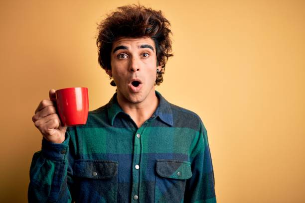 istock Young handsome man drinking cup of coffee standing over isolated yellow background scared in shock with a surprise face, afraid and excited with fear expression 1212518382