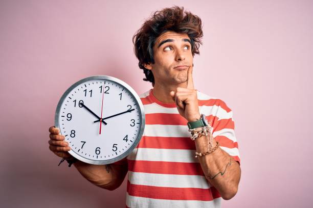 istock Young handsome man holding big clock standing over isolated pink background serious face thinking about question, very confused idea 1212519574