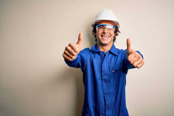 istock Young constructor man wearing uniform and security helmet over isolated white background approving doing positive gesture with hand, thumbs up smiling and happy for success. Winner gesture. 1212519941