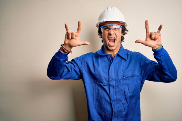 istock Young constructor man wearing uniform and security helmet over isolated white background shouting with crazy expression doing rock symbol with hands up. Music star. Heavy concept. 1212519944