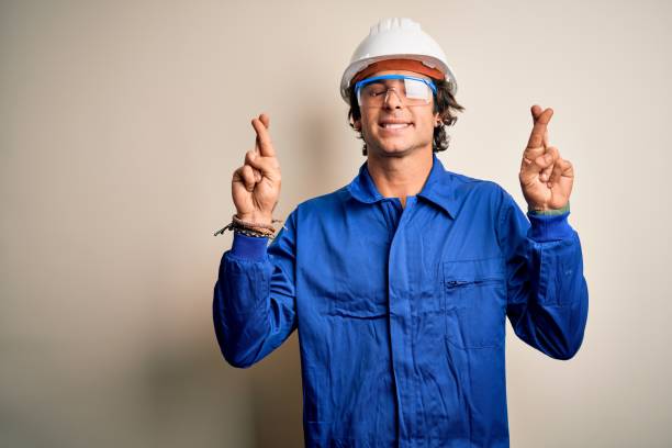 istock Young constructor man wearing uniform and security helmet over isolated white background gesturing finger crossed smiling with hope and eyes closed. Luck and superstitious concept. 1212519958