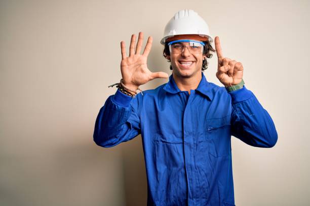 istock Young constructor man wearing uniform and security helmet over isolated white background showing and pointing up with fingers number six while smiling confident and happy. 1212519985