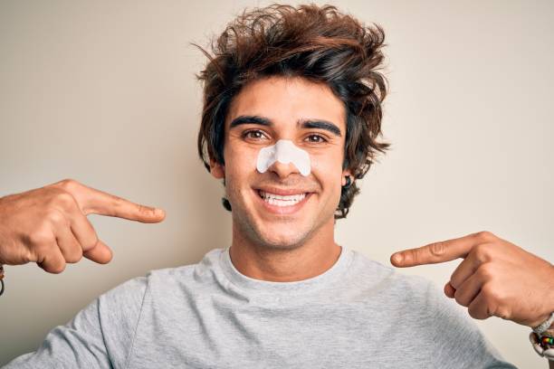 istock Young handsome man using nose strip standing over isolated white background looking confident with smile on face, pointing oneself with fingers proud and happy. 1212520042