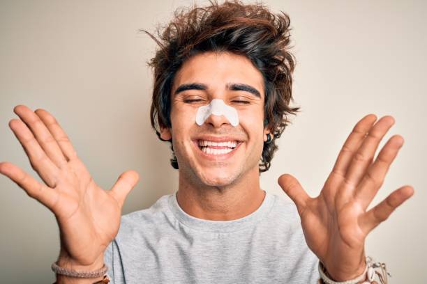 istock Young handsome man using nose strip standing over isolated white background celebrating mad and crazy for success with arms raised and closed eyes screaming excited. Winner concept 1212520045