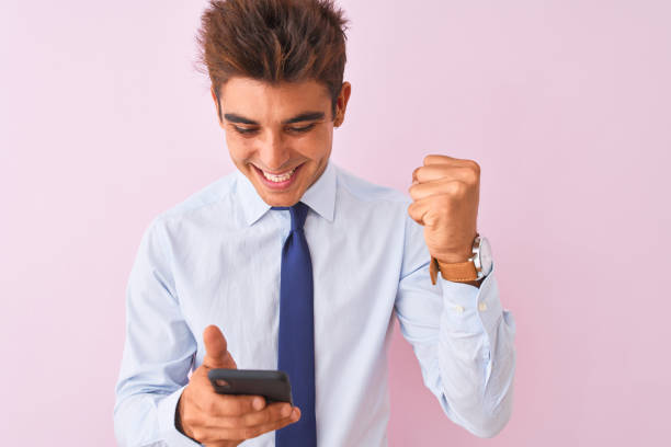 istock Young handsome businessman using smartphone standing over isolated pink background screaming proud and celebrating victory and success very excited, cheering emotion 1212520278