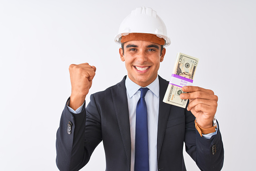 Young handsome architect man wearing helmet holding dollars over isolated white background screaming proud and celebrating victory and success very excited, cheering emotion