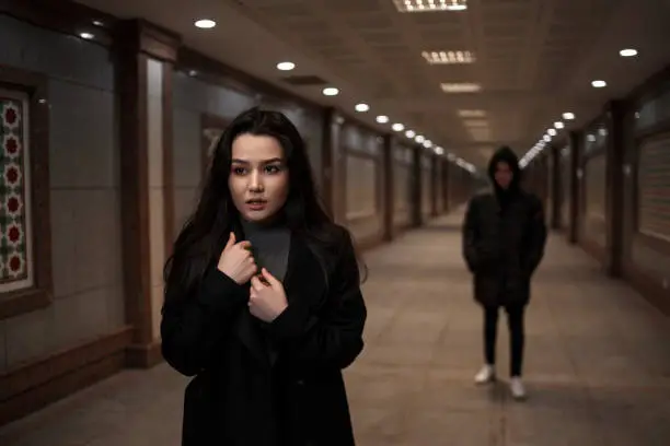 Photo of a young beautiful woman walks, followed by a man in dark clothes with a hood on his head. mosaics on the walls are not someone's works of art.these are walls in Underpass in an Oriental style