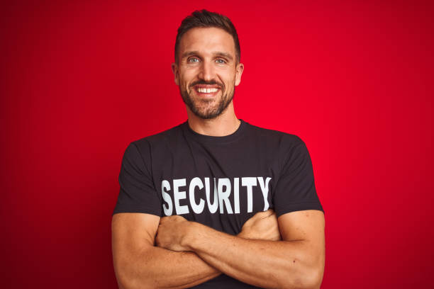 istock Young safeguard man wearing security uniform over red isolated background happy face smiling with crossed arms looking at the camera. Positive person. 1212524694