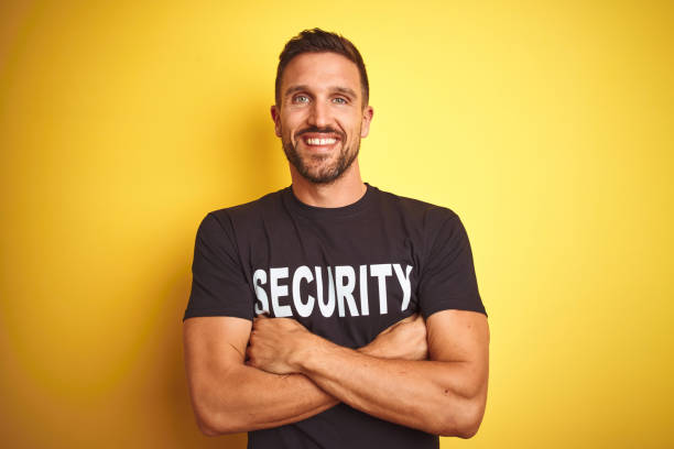 istock Young safeguard man wearing security uniform over yellow isolated background happy face smiling with crossed arms looking at the camera. Positive person. 1212524728