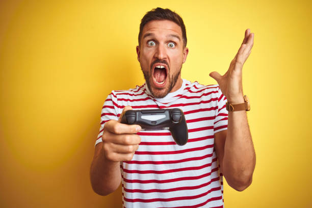 istock Young handsome man playing video games using joystick game pad over yellow background very happy and excited, winner expression celebrating victory screaming with big smile and raised hands 1212527402