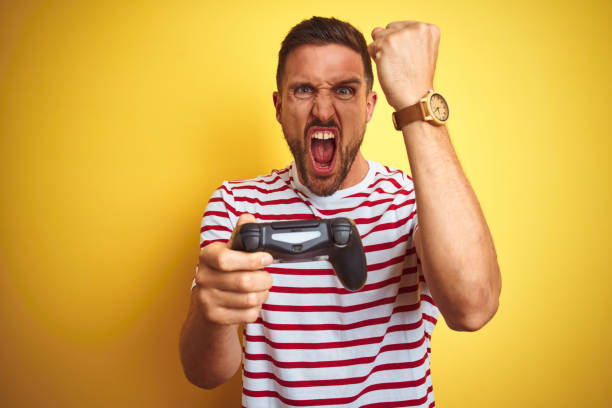 istock Young handsome man playing video games using joystick game pad over yellow background annoyed and frustrated shouting with anger, crazy and yelling with raised hand, anger concept 1212527682