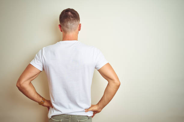 young handsome man wearing casual white t-shirt over isolated background standing backwards looking away with arms on body - over the shoulder view fotos imagens e fotografias de stock