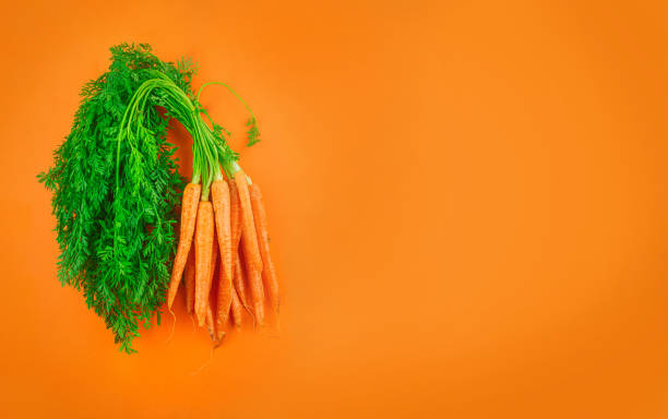 istock Bunch of carrots on an orange background 1212529780