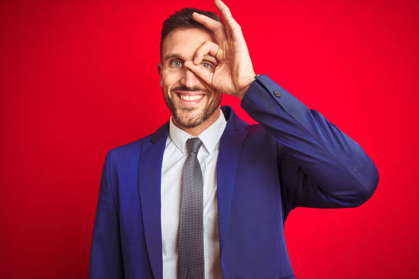 istock Young handsome business man over red isolated background doing ok gesture with hand smiling, eye looking through fingers with happy face. 1212530454