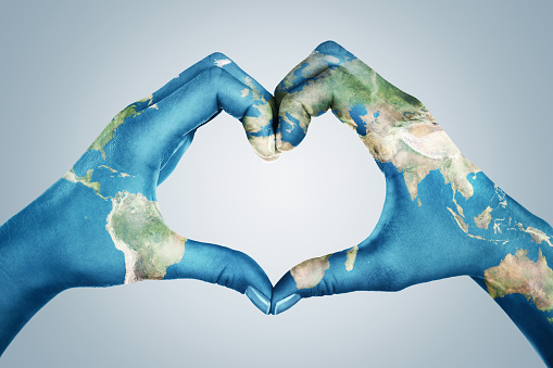 Female hands, painted in the world map,  forming heart shape isolated on blue background. Element of this image furnished by NASA ( https://earthobservatory.nasa.gov/blogs/elegantfigures/2011/10/06/crafting-the-blue-marble/ )
