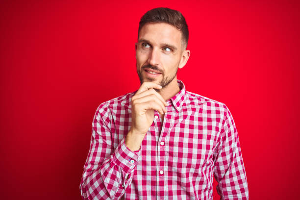 istock Young handsome man over red isolated background with hand on chin thinking about question, pensive expression. Smiling and thoughtful face. Doubt concept. 1212531277