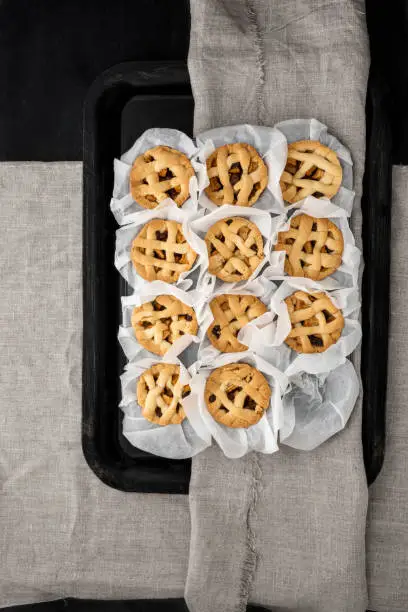 Eleven mini homemade apple pie in white baking paper on a scratched black tray with natural linen