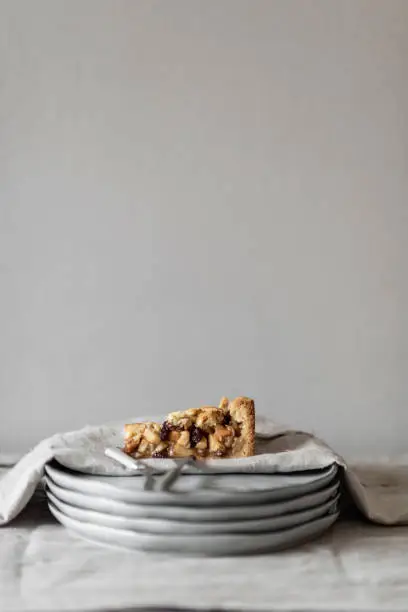 Piece of Dutch home made applepie on a stack of light grey plates on white linen