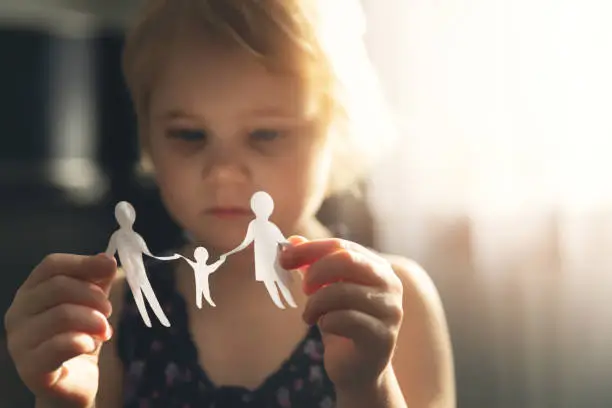 Photo of little girl with paper family in hands. concept of divorce, custody and child abuse