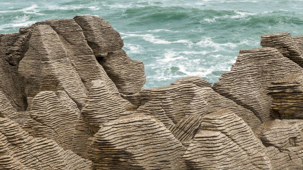 Pancake rocks along the coast of South Island, New Zealand, near Punakaiki. Close-up of the rocks; sea in the distance. Pancake rocks along the coast of South Island, New Zealand, near Punakaiki. Close-up of the rocks; sea in the distance. Pancake Rocks has irregular chasms and ridges, typical of limestone country. The layers of resistant bands of limestone are separated by softer, thin, mud-rich layers. This type of layering, found in limestones worldwide, is called stylobedding. punakaiki stock pictures, royalty-free photos & images