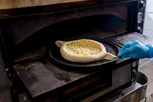 Chef cooking khachapuri with cheese and egg. Georgian national cuisine. Restaurant. Background