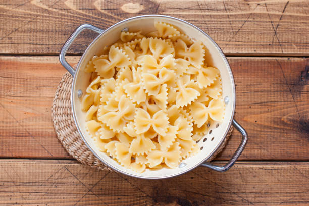 istock Step by step preparation of Farfalle with fried chicken liver and carrots, step 3 - cooked farfalle in a colander top view, horizontal 1212543173