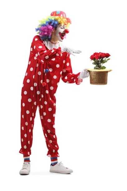 Full length shot of a clown holding a hat with red roses inside isolated on white background