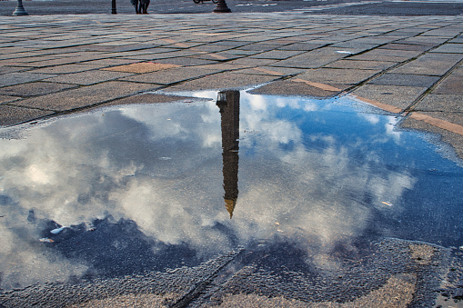 Paris, France - March 12, 2020 - View of the streets of Paris in the rain. In the foreground, a puddle of rain surrounded by paving stones on the Place de la Concorde in Paris turns into a mirror reflecting the top of the obelisk. In the background, a second puddle reflects another piece of the obelisk