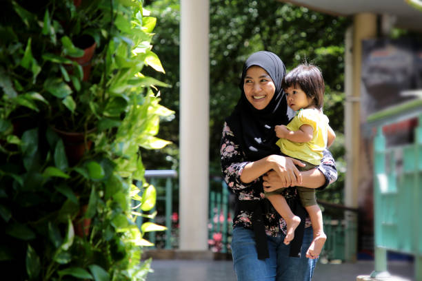 A modern Muslim female adult is carrying her toddler daughter and spending outdoor bonding time in Malaysia.