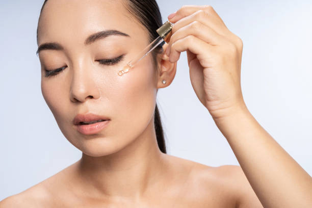 Asian beautiful female is applying eye serum Close up of pretty lady putting anti-ageing moisturizing serum to under eye area. Beauty therapy concept face serum stock pictures, royalty-free photos & images