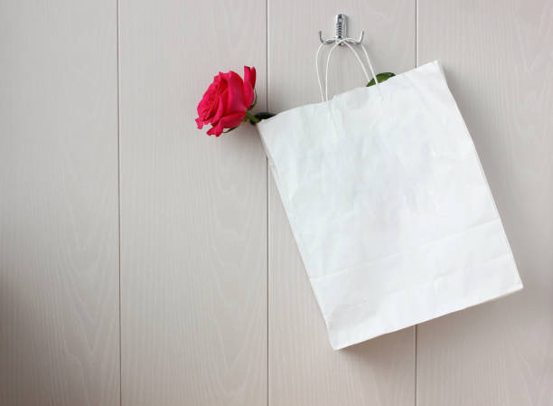 istock pink rose in a paper bag on a hook on a light wall. 1212560884