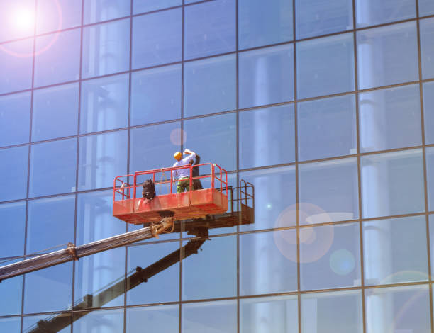 Working window cleaner on a telescopic platform washes the Windows of a modern skyscraper, work with high risk Working window cleaner on a telescopic platform washes the Windows of a modern skyscraper, work with high risk. muster station stock pictures, royalty-free photos & images