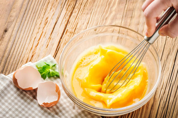 istock Woman whisking eggs. Wipped eggs in glass bowl with broken empty egg 1212565746