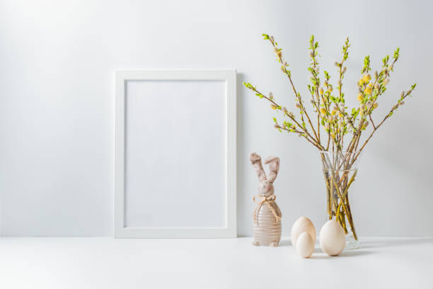 istock Home interior with easter decor. Mockup with a white frame and willow branches in a vase on a light background 1212568161