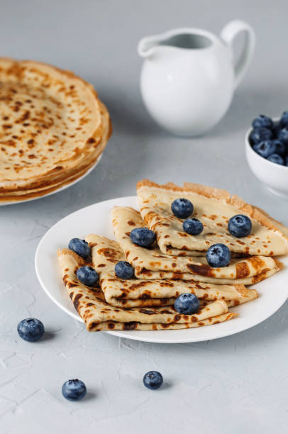 istock Thin pancakes on white plate with blueberries and sour cream. Grey background. Close up. 1212568234