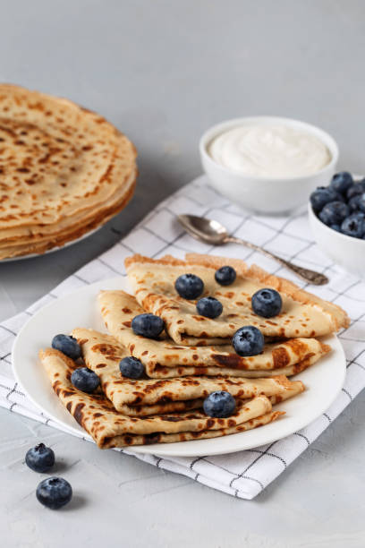 istock Thin pancakes on white plate with blueberries and sour cream. Served with a 1212568236