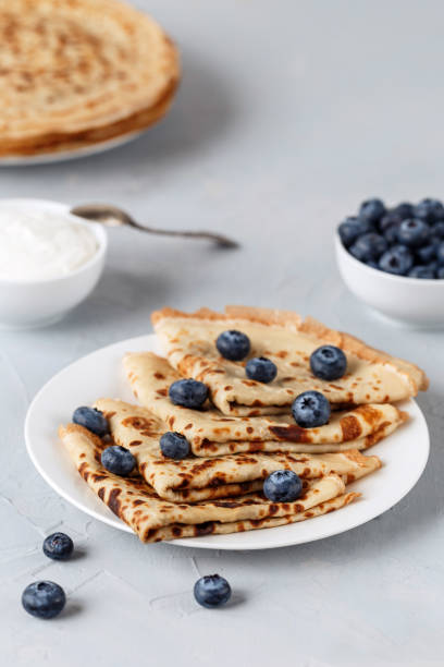 istock Four thin pancakes on white plate with blueberries and sour cream. Grey background. 1212568261