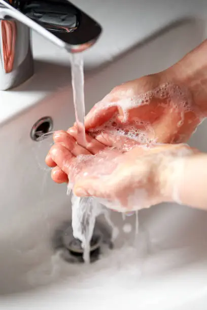 woman washing hands with antibacterial soap under running water.