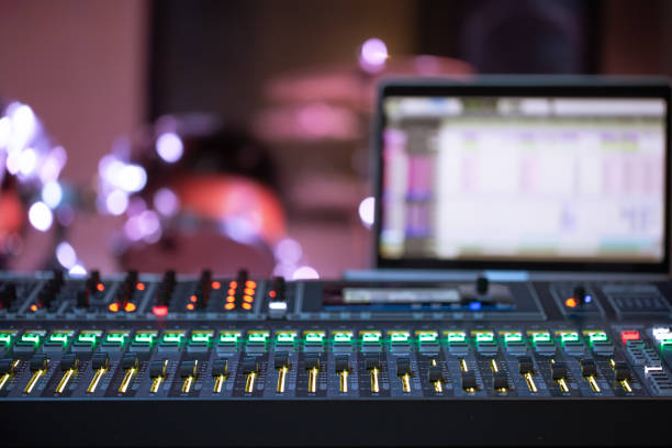 A sound mixer and laptop sit on a table, with a crowd watching an event in the background of a gymnasium.
