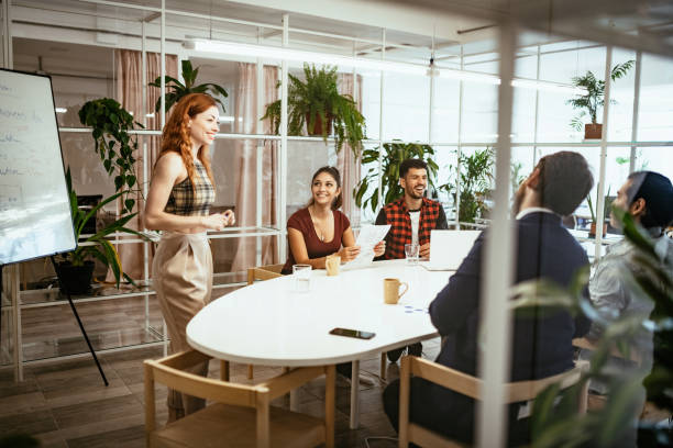 Redhead Latina presenting analysis to colleagues in eco-friendly office Latin businesswoman in office with colleagues, having presentation of business results synergy series stock pictures, royalty-free photos & images