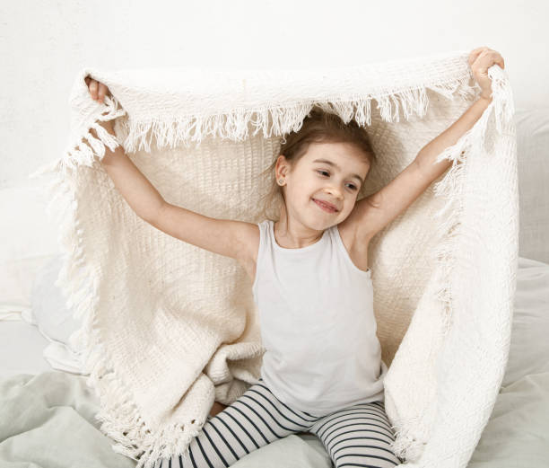 istock Cute little girl playing in bed with a blanket. 1212576435