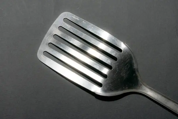 Close up of a metallic kitchen spatula on grey background