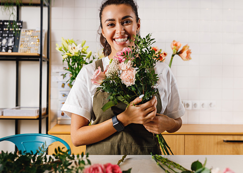 Portrait of a beautiful woman florist holding a bouquet and looking at camera in a flower shop