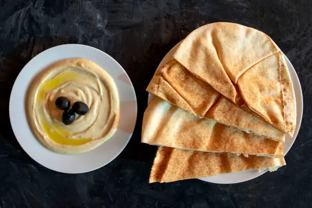 Photo of Tahini sauce and pita bread on dark gray rustic background.